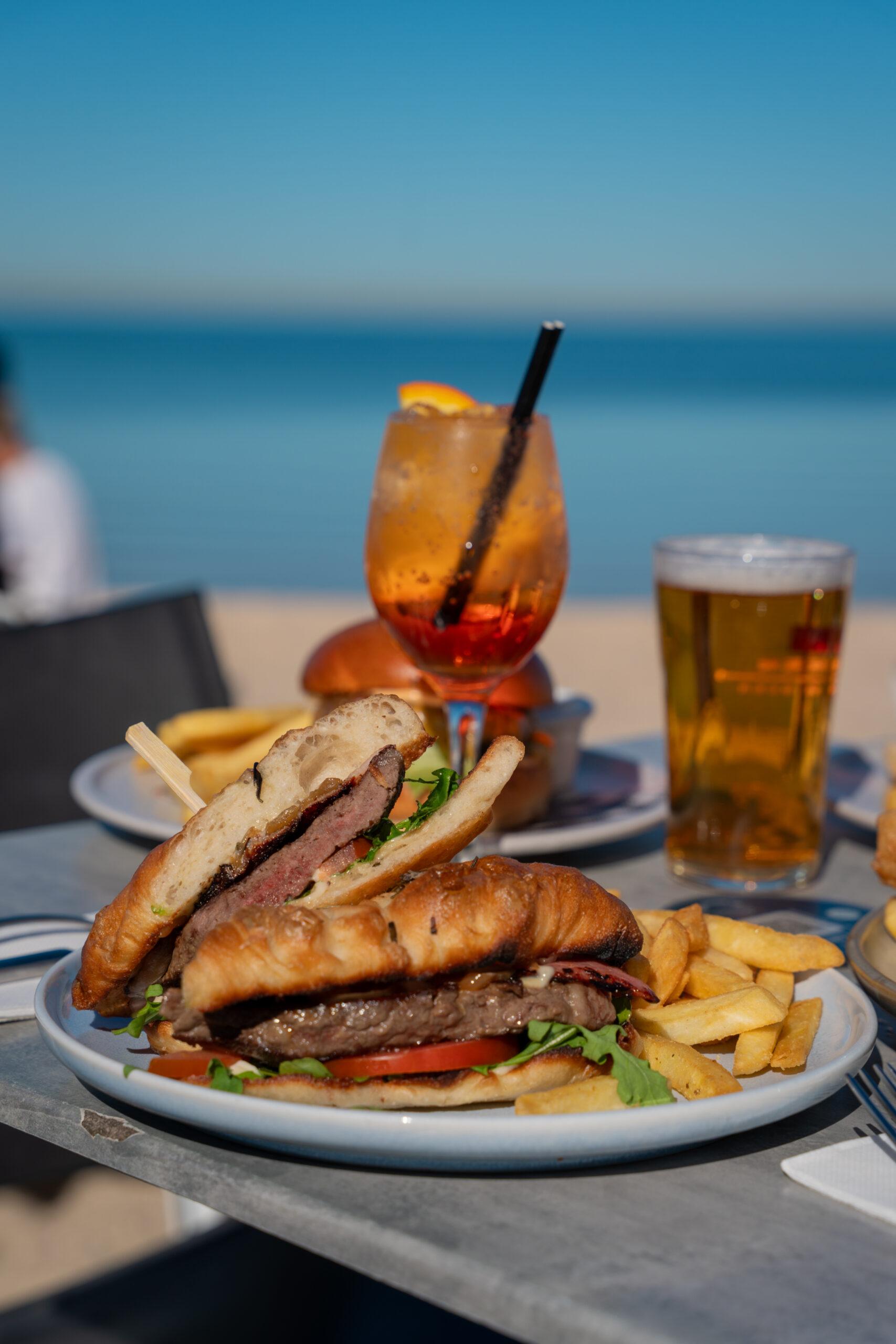 Steak sandwich with 150g medium-rare porterhouse, bacon, tomato, rocket, caramelised onion, and aioli in toasted focaccia, served with chips.