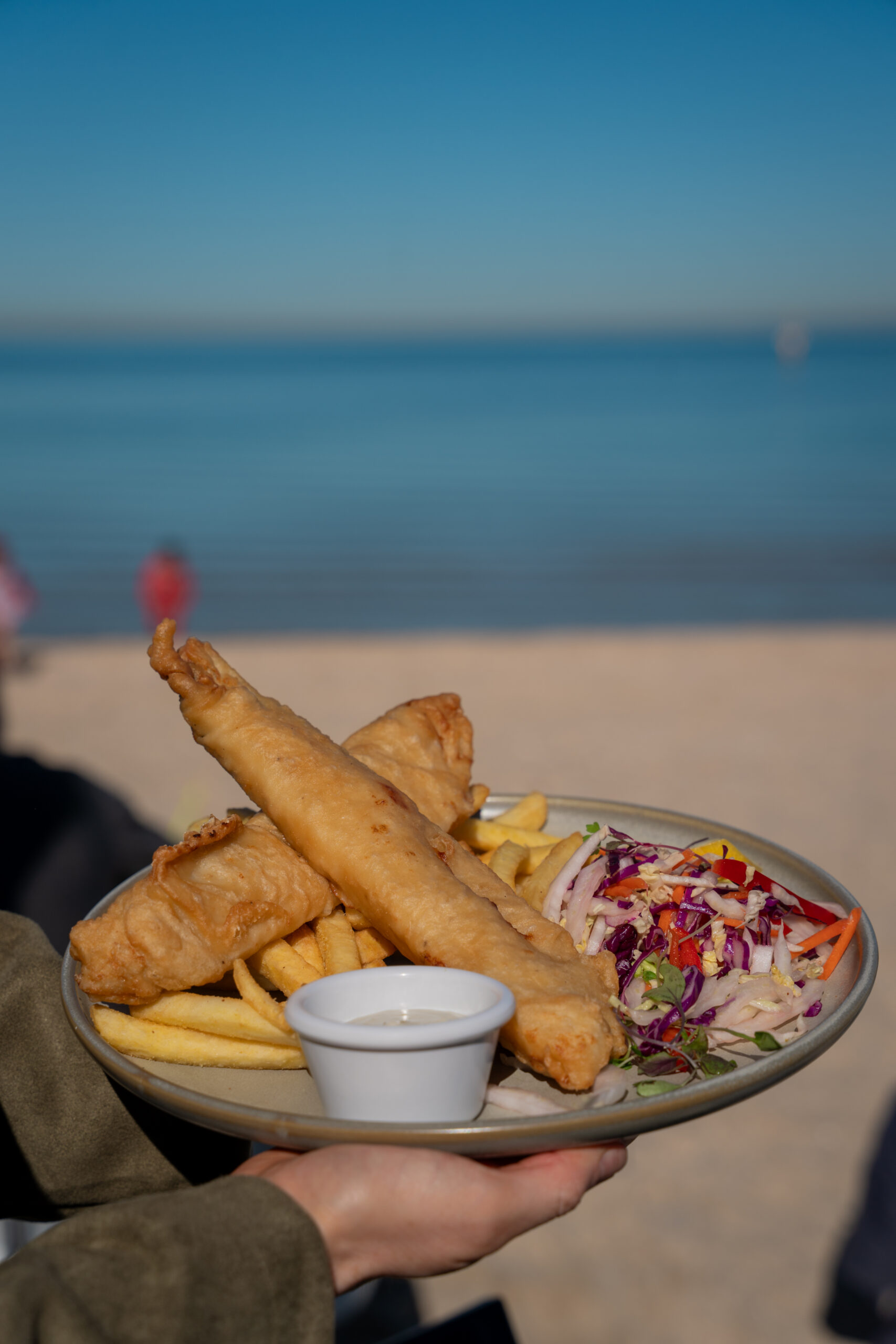 Menu item at the Sandbar Middle Park - Beer battered barramundi with salt and vinegar seasoning, served with golden chips, rainbow slaw, tartare sauce, and lemon
